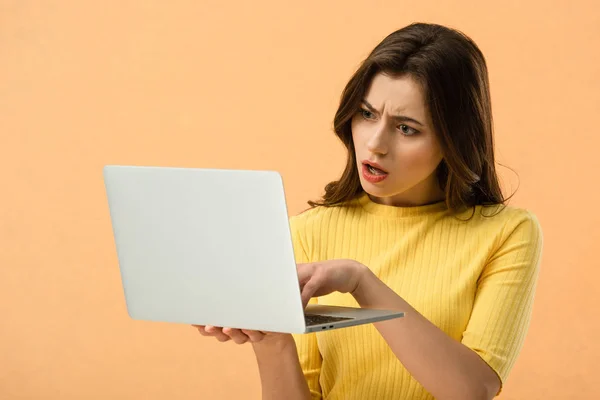 Dissatisfied brunette young woman using laptop isolated on orange — Stock Photo