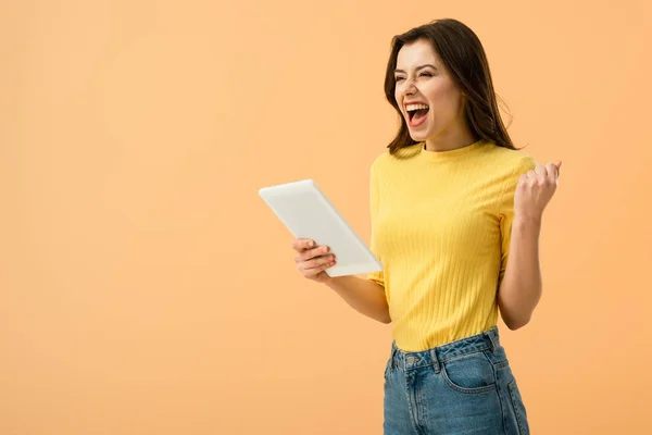 Aufgeregtes brünettes Mädchen hält digitales Tablet in der Hand und lacht isoliert auf orange — Stockfoto