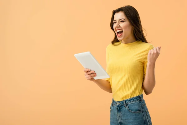 Emocionado chica morena sosteniendo tableta digital y riendo aislado en naranja - foto de stock