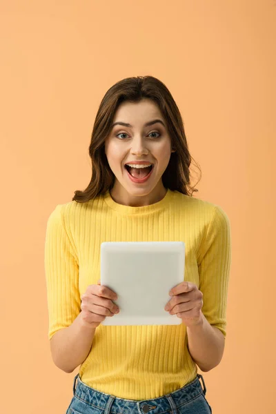 Front view of happy brunette girl holding digital tablet and laughing isolated on orange — Stock Photo