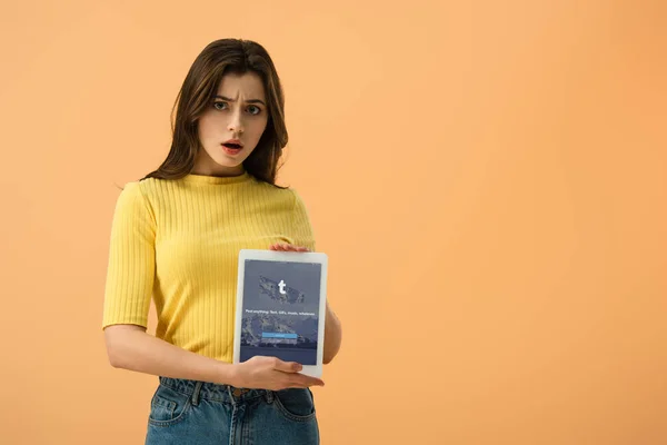 Ragazza bruna insoddisfatta con tablet digitale con app tumblr sullo schermo isolato su arancione — Foto stock