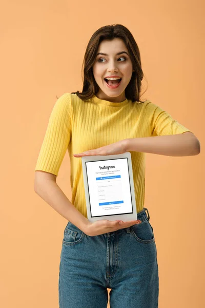 Возбужденная брюнетка с цифровым планшетом с приложением Instagram на экране изолированы на оранжевый — стоковое фото