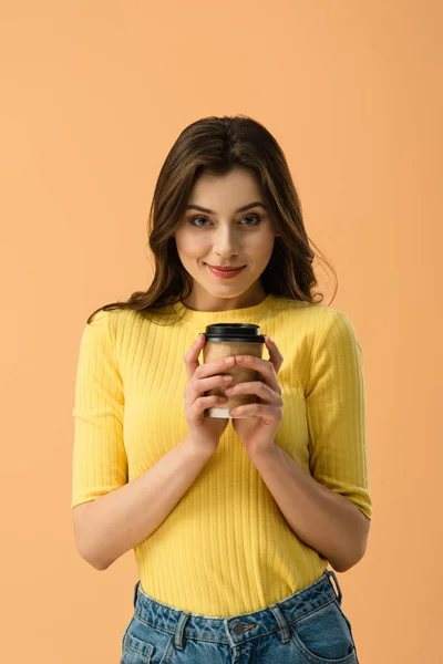 Front view of tricky brunette girl holding paper cup of coffee isolated on orange — Stock Photo