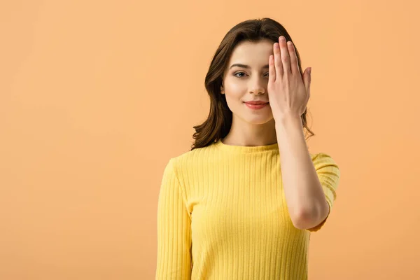 Alegre joven mujer cubriendo ojo con la mano aislada en naranja - foto de stock