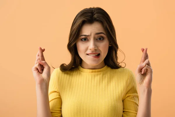 Attrayant brunette femme mordant lèvres tandis que debout avec les doigts croisés isolé sur orange — Photo de stock