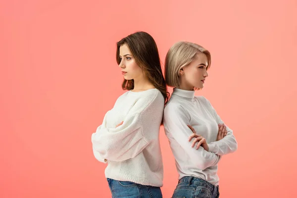 Atractiva chica morena de pie cerca de un amigo rubio con brazos cruzados aislados en rosa - foto de stock