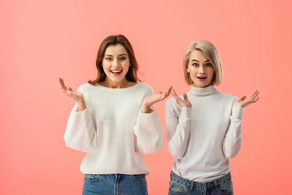 Attractive brunette and blonde girls showing shrug gesture isolated on pink — Stock Photo
