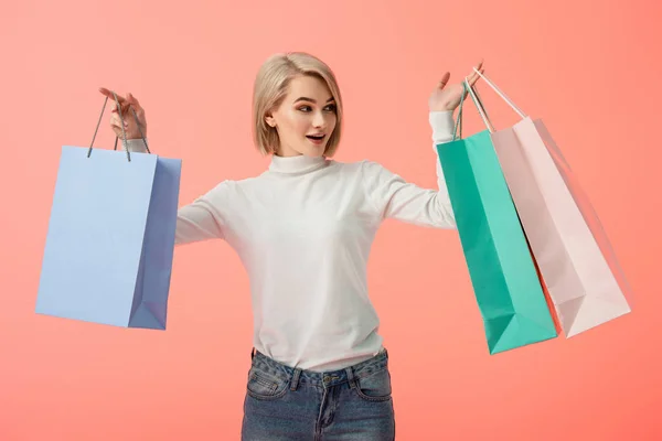 Überrascht blonde junge Frau mit Einkaufstaschen isoliert auf rosa — Stockfoto
