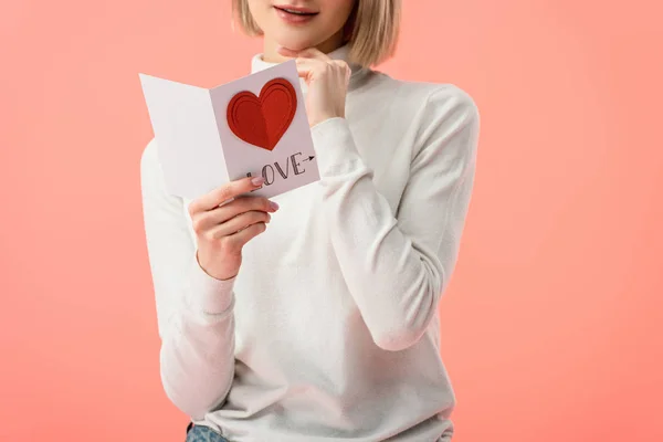 Vista recortada de la mujer que sostiene la tarjeta de felicitación mientras está de pie aislado en rosa - foto de stock