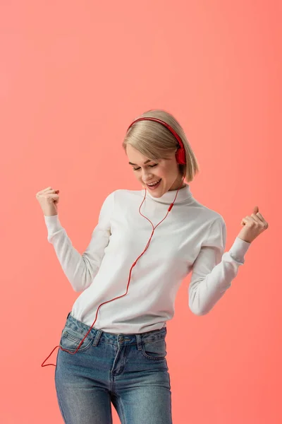 Allegra donna bionda ascoltando musica in cuffia e gesticolando isolato su rosa — Foto stock