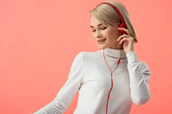 Happy blonde young woman listening music in headphones isolated on pink — Stock Photo