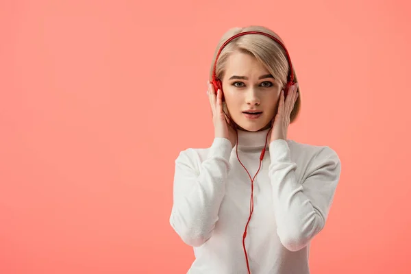 Mujer joven rubia sorprendida escuchando música en auriculares aislados en rosa - foto de stock