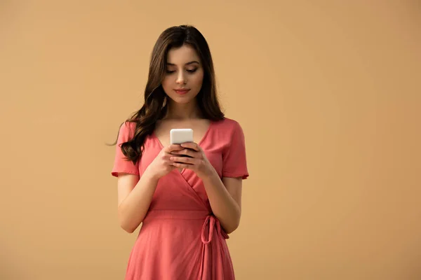 Happy brunette girl using smartphone while standing isolated on brown — Stock Photo