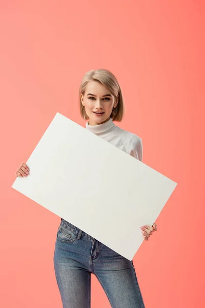 Heureuse blonde fille tenant placard vierge isolé sur rose — Photo de stock