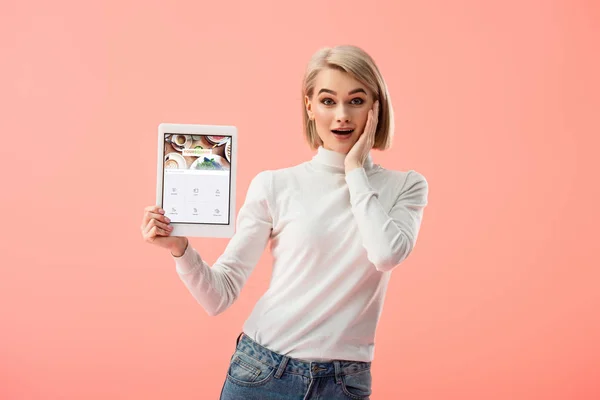 Здивований блондинка Жінка тримає Цифрова табличка з квадрат app на екрані ізольовані на рожевий — стокове фото