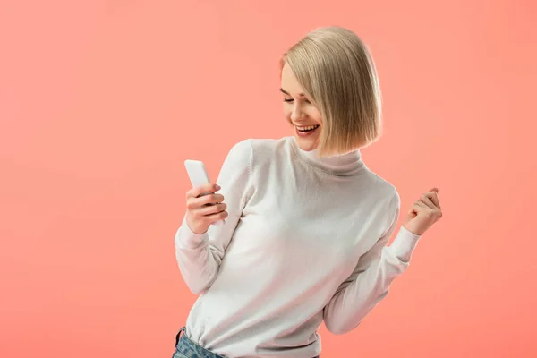 Cheerful blonde girl using smartphone isolated on pink — Stock Photo