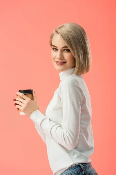 Happy blonde girl holding paper cup with drink isolated on pink — Stock Photo