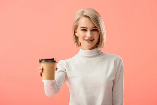 Selektiver Fokus des fröhlichen blonden Mädchens mit Pappbecher und Getränk isoliert auf rosa — Stockfoto