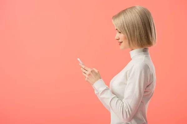 Seitenansicht der attraktiven blonden Frau mit Smartphone isoliert auf rosa — Stockfoto