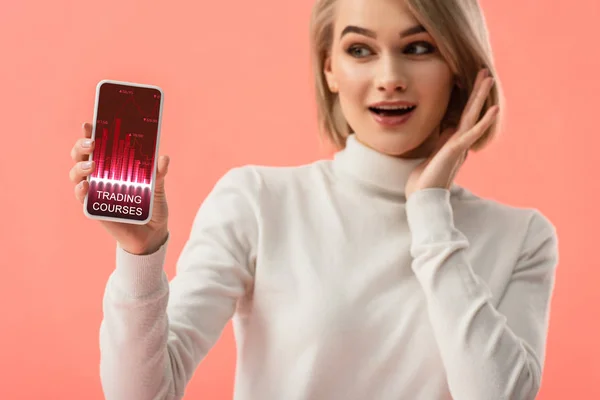 Selective focus of surprised blonde woman holding smartphone with graphs on screen isolated on pink — Stock Photo