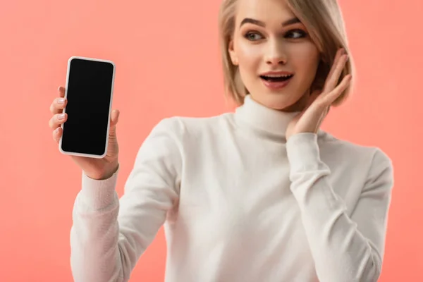 Enfoque selectivo de impactada joven rubia sosteniendo teléfono inteligente con pantalla en blanco aislado en rosa - foto de stock