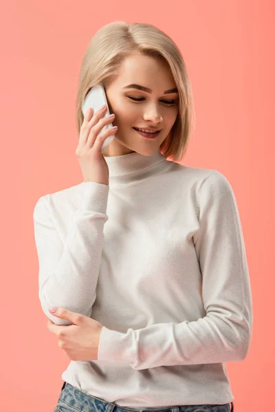 Atractiva mujer rubia hablando en el teléfono inteligente aislado en rosa - foto de stock
