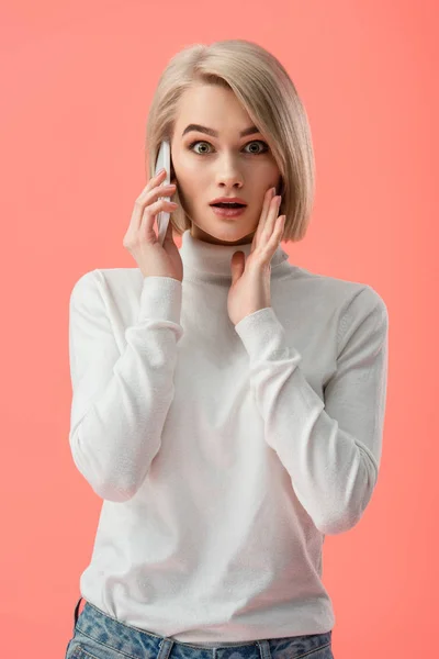 Mujer rubia impactada hablando en el teléfono inteligente aislado en rosa - foto de stock