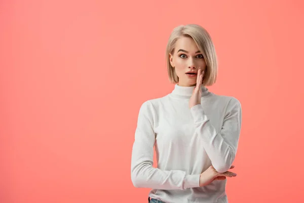 Shocked blonde girl standing and looking at camera isolated on pink — Stock Photo