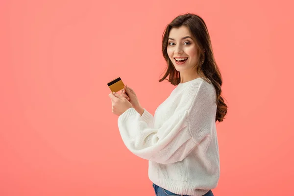 Happy brunette girl holding credit card isolated on pink — Stock Photo