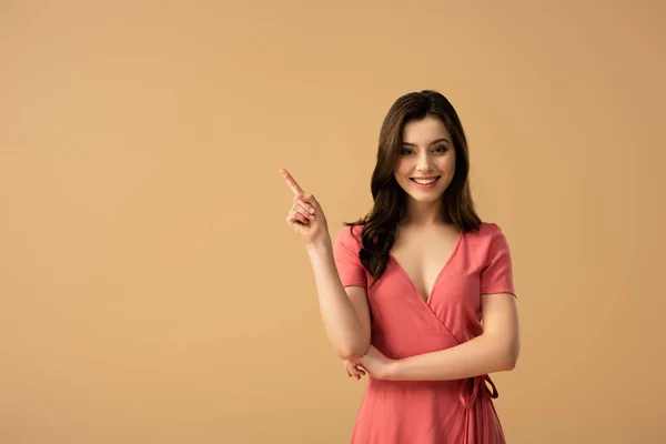 Cheerful brunette woman pointing with finger while standing isolated on brown — Stock Photo