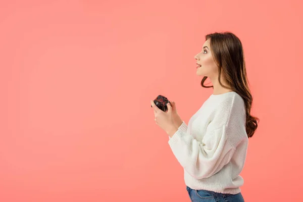 Vista laterale della ragazza sorpresa tenendo joystick mentre in piedi isolato su rosa — Foto stock