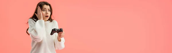 Panoramic shot of shocked girl holding joystick while standing isolated on pink — Stock Photo