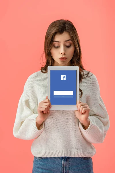 Приваблива молода жінка тримає Цифрова табличка з facebook app на екрані ізольовані на рожевий — стокове фото