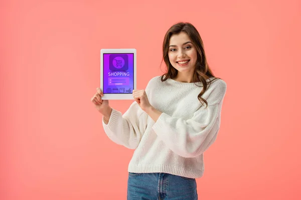 Веселая молодая женщина держит цифровой планшет с приложением для покупок на экране изолированы на розовый — стоковое фото