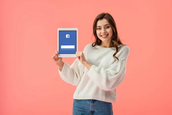 Alegre joven mujer sosteniendo tableta digital con aplicación de facebook en la pantalla aislado en rosa - foto de stock