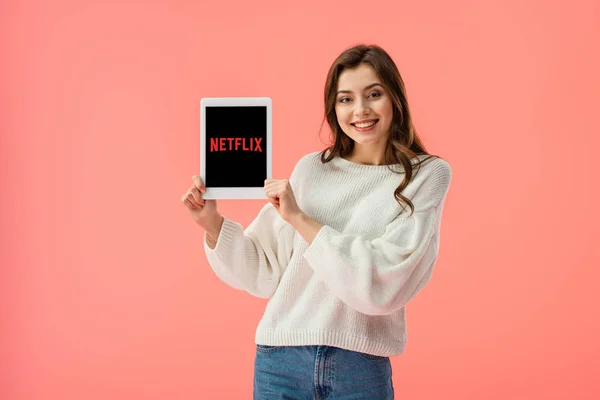 Cheerful young woman holding digital tablet with netflix app on screen isolated on pink — Stock Photo