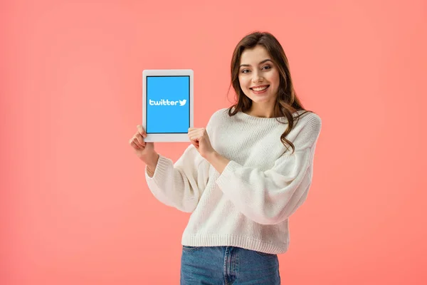 Feliz joven sosteniendo la tableta digital con la aplicación de twitter en la pantalla aislada en rosa - foto de stock