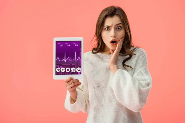Schockierte junge Frau hält digitales Tablet mit Gesundheits-App auf dem Bildschirm isoliert auf rosa — Stockfoto