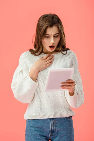 Shocked and beautiful young woman holding digital tablet isolated on pink — Stock Photo