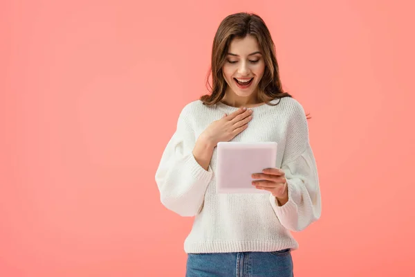 Mujer joven sorprendida y atractiva sosteniendo tableta digital aislada en rosa - foto de stock