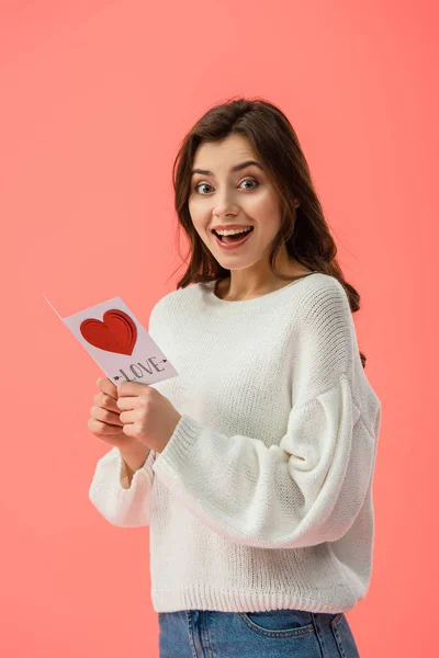 Überrascht und schöne junge Frau mit Karte mit Liebe Schriftzug isoliert auf rosa — Stockfoto