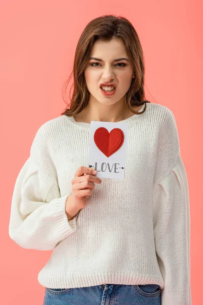 Angry young woman holding card with love lettering isolated on pink — Stock Photo