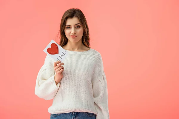 Traurige junge Frau hält Karte mit Liebesaufdruck auf rosa — Stockfoto