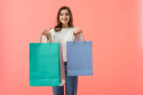 Smiling woman in white sweater and jeans holding shopping bags isolated on pink — Stock Photo