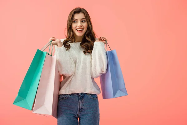 Mujer sonriente y atractiva en suéter blanco sosteniendo bolsas aisladas en rosa - foto de stock