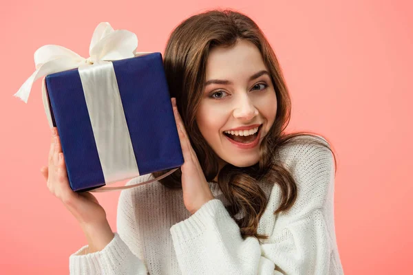 Smiling and beautiful woman in white sweater holding gift box isolated on pink — Stock Photo