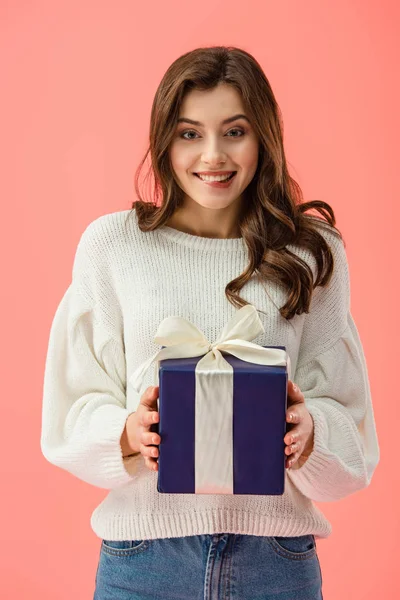 Усміхнена і приваблива жінка в білому светрі тримає подарункову коробку ізольовано на рожевому — стокове фото