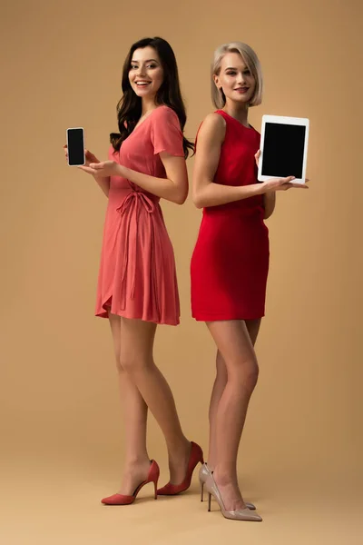 Pleine longueur de femmes en robes rouges tenant smartphone et tablette numérique avec espace de copie — Photo de stock