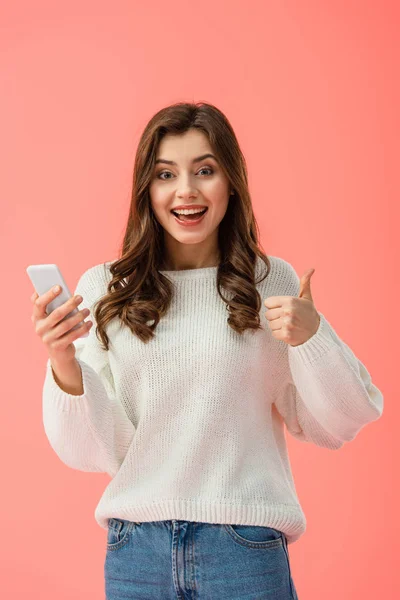 Mulher sorridente e atraente com polegar para cima segurando smartphone isolado em rosa — Fotografia de Stock