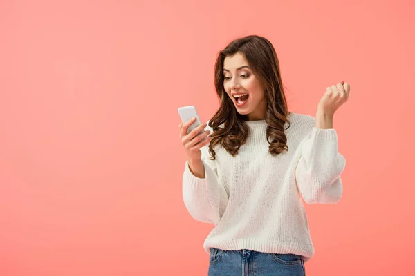 Mujer sorprendida y atractiva en suéter blanco sosteniendo teléfono inteligente aislado en rosa - foto de stock